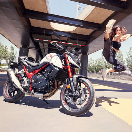 Egy női táncosnő a levegőbe ugrik a Honda CB750 Hornet mellett.