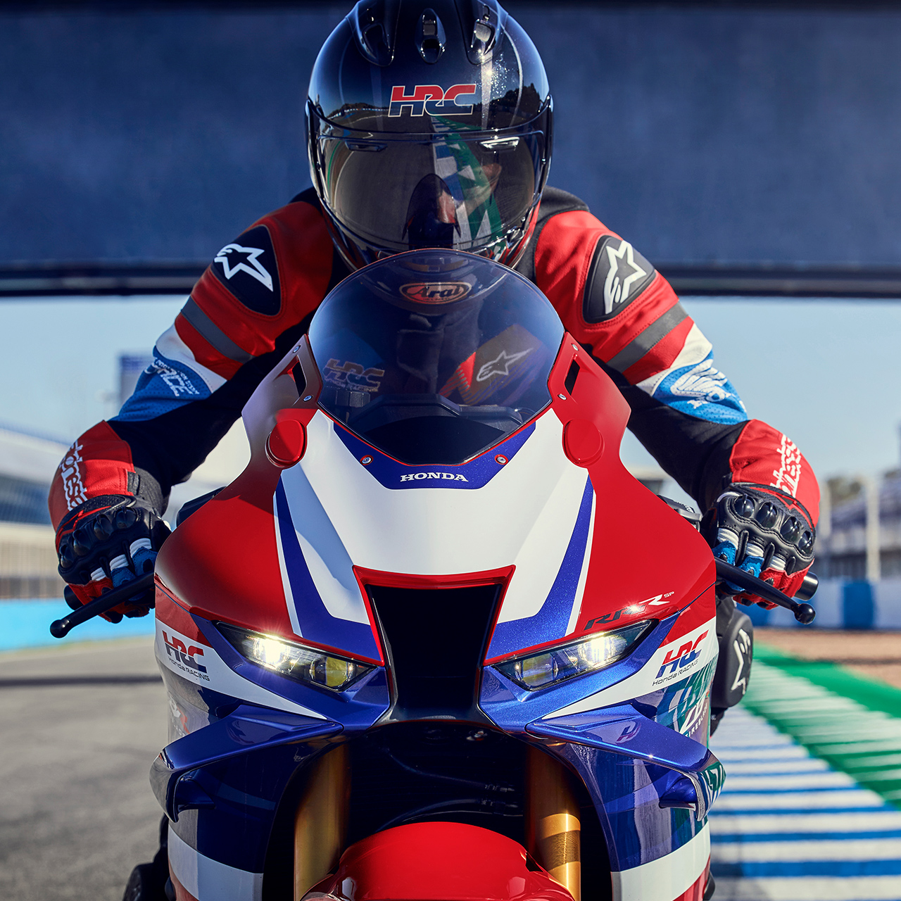 Közeli kép: szemből látható motoros a Honda CBR1000rr-r Fireblade nyergében, versenypályán. 
