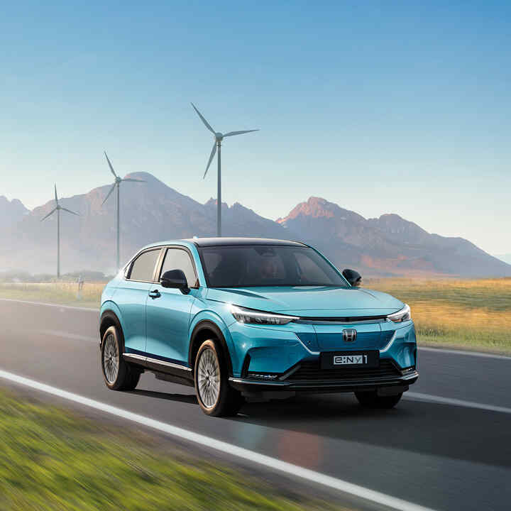 Egy Honda e:Ny1 és egy Honda e modell halad el egy szélerőműpark mellett. 
