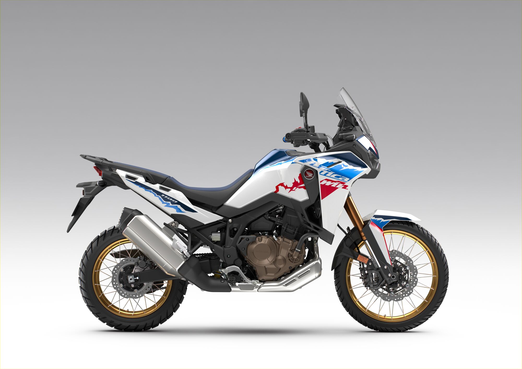 A side view of a Honda Africa Twin adventure motorcycle in white, blue, and red color scheme with gold wheels against a light gray background.