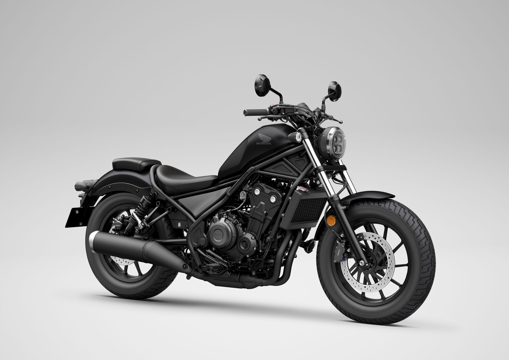 A black Honda Rebel 500 motorcycle in profile view against a light background. The bike features a sleek, modern cruiser design with a round headlight, low-slung seat, and blacked-out components.